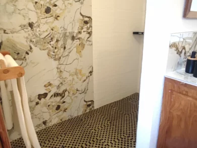 Le Campement Houéfa compte deux villas, avec chacune 3 chambres. Photo du vaste espace douche de la chambre numéro 1. Douche à l'italienne, mosaïques de couleur noir et or au sol, porte serviettes.