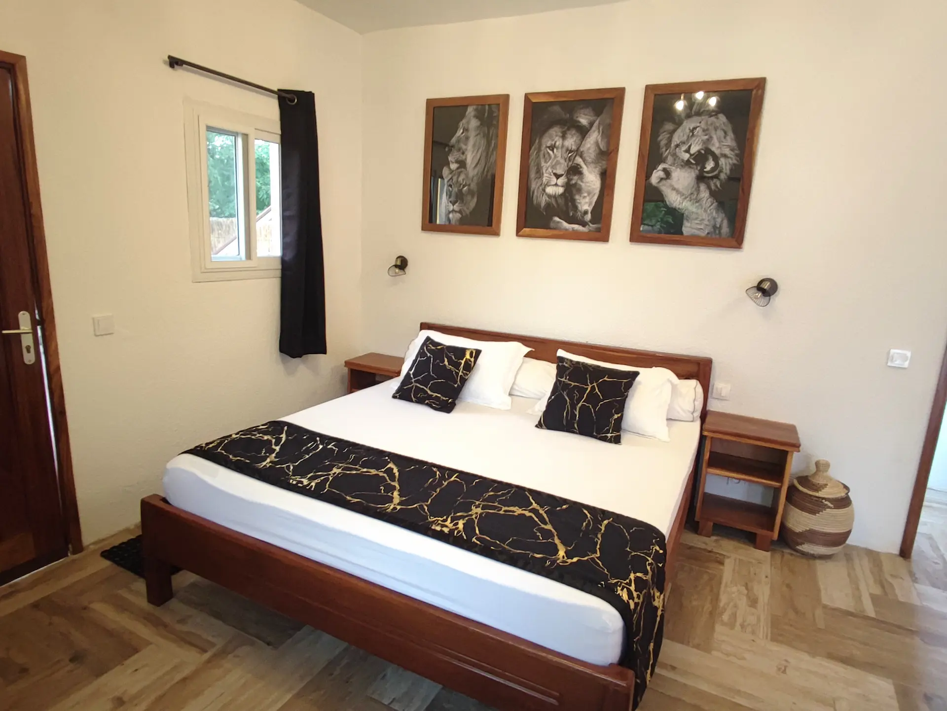 Le Campement Houéfa compte deux villas, avec chacune 3 chambres. Photo de la chambre numéro 1 avec son lit King size drapé de blanc, d'un chemin de lit et de coussins d'apparat de couleur noir et or, rappelant avec élégance les tons de l'espace douche et du triptyque surplombant le lit.