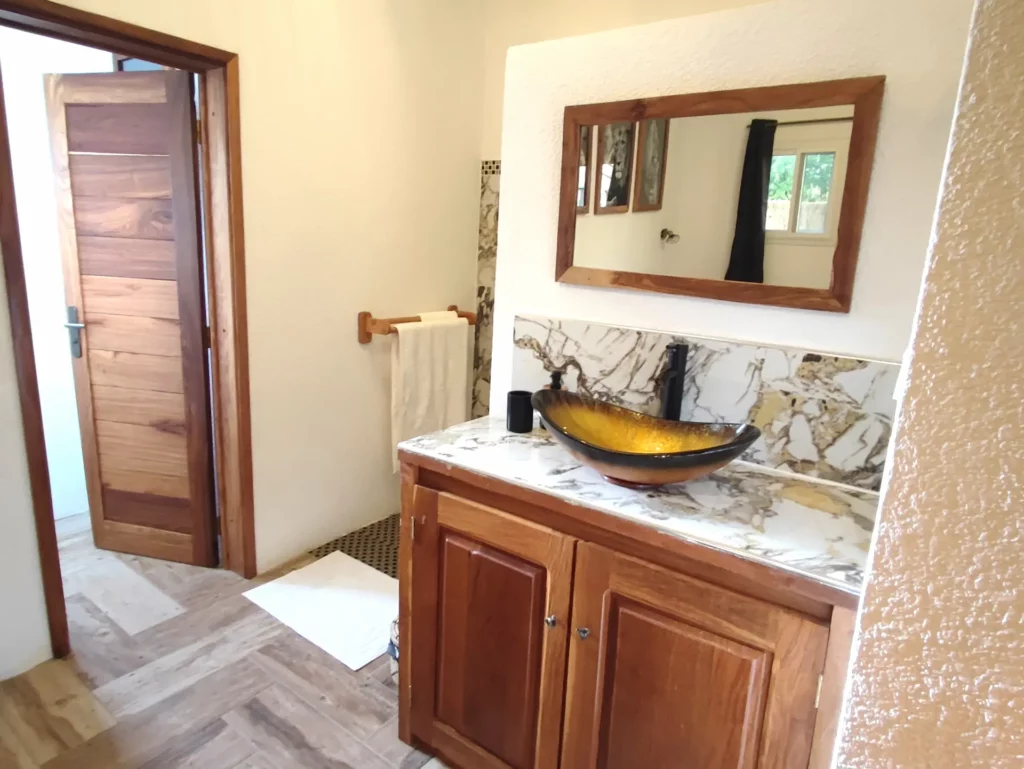 Le Campement Houéfa compte deux villas, avec chacune 3 chambres. Photo de la vasque noire et or de la chambre numéro 1 et son carrelage rappelant le marbre. Un miroir mural positionné à l'horizontal, au-dessus du meuble vasque complète l'équipement de l'espace salle de bain.