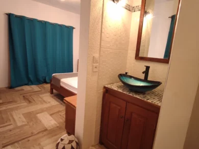 Photo de la chambre numéro 2, située au rez-de-chaussée de la première villa. L'espace nuit est séparé de l'espace salle de bain par un couloir menant au cabinet de toilette. Le tout est très lumineux, pouvant être occulté par d'amples rideaux de couleur bleu azur.