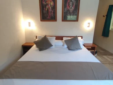 Le Campement Houéfa compte deux villas, avec chacune 3 chambres. Photo de la chambre numéro 2 avec son diptyque représentant deux des Big Five, son lit King size, son chemin de lit et ses coussins d'apparat rappelant subtilement le code couleur de l'espace salle de bain.