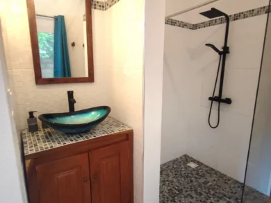 Le Campement Houéfa compte deux villas, avec chacune 3 chambres. Photo de l'espace salle de bain de la chambre numéro 2 avec sa vasque couleur azur, son miroir mural vertical au-dessus du meuble sous-vasque.