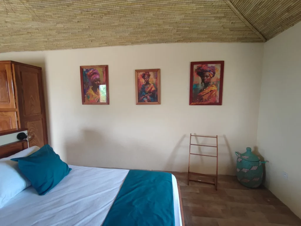 Le Campement Houéfa compte deux villas, avec chacune 3 chambres. Photo de la chambre numéro 3 avec ses beaux portraits de femmes africaines, son plafond en boudins de palmier rônier, son lit King size et son mobilier en bois fabriqué localement.