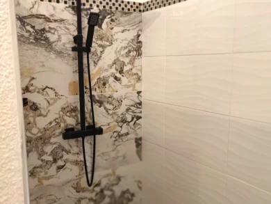 Photo du vaste espace douche de la chambre numéro 5. Douche à l'italienne, carrelage blanc et rappelant le marbre, avec mosaïque noir et or.