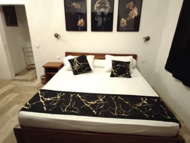 Le Campement Houéfa compte deux villas, avec chacune 3 chambres. Photo de la chambre numéro 5 avec son triptyque, portait d'une femme parée de bijoux en or, son lit King size, son chemin de lit et ses coussins d'apparat rappelant subtilement le code couleur de cette chambre.