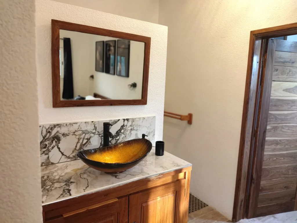 Le Campement Houéfa compte deux villas, avec chacune 3 chambres. Photo de la vasque noire et or de la chambre numéro 5 et son carrelage rappelant le marbre. Un miroir mural positionné à l'horizontal, au-dessus du meuble vasque complète l'équipement de l'espace salle de bain.