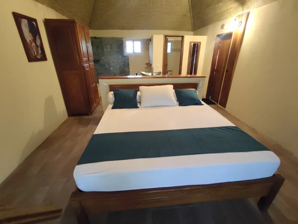 Vue d'ensemble de la chambre numéro 6, située à l'étage de la seconde villa, dotée d'un lit King size, d'une literie confortable, d'une douche à l'italienne, d'un meuble salle de bain avec vasque, d'un cabinet de toilette séparé, d'une commode, d'une grande armoire, de luminaires et d'un miroir mural.