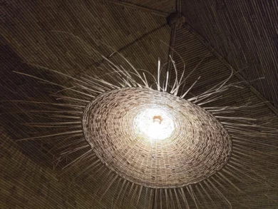 Le Campement Houéfa compte deux villas, avec chacune 3 chambres. Photo de la suspension lumineuse de la chambre numéro 6. Tressée en paille, elle est le fruit de l'artisanat local et reprend subtilement la couleur des boudins de palmier rônier habillant le plafond de la chambre.