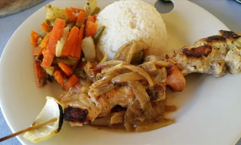 A proximité du Campement Houéfa, vous pourrez déguster des plats traditionnels sénégalais voire gastronomiques. L'image représente une brochette de lotte avec sauce yassa accompagnée de riz blanc et de légumes sautés.